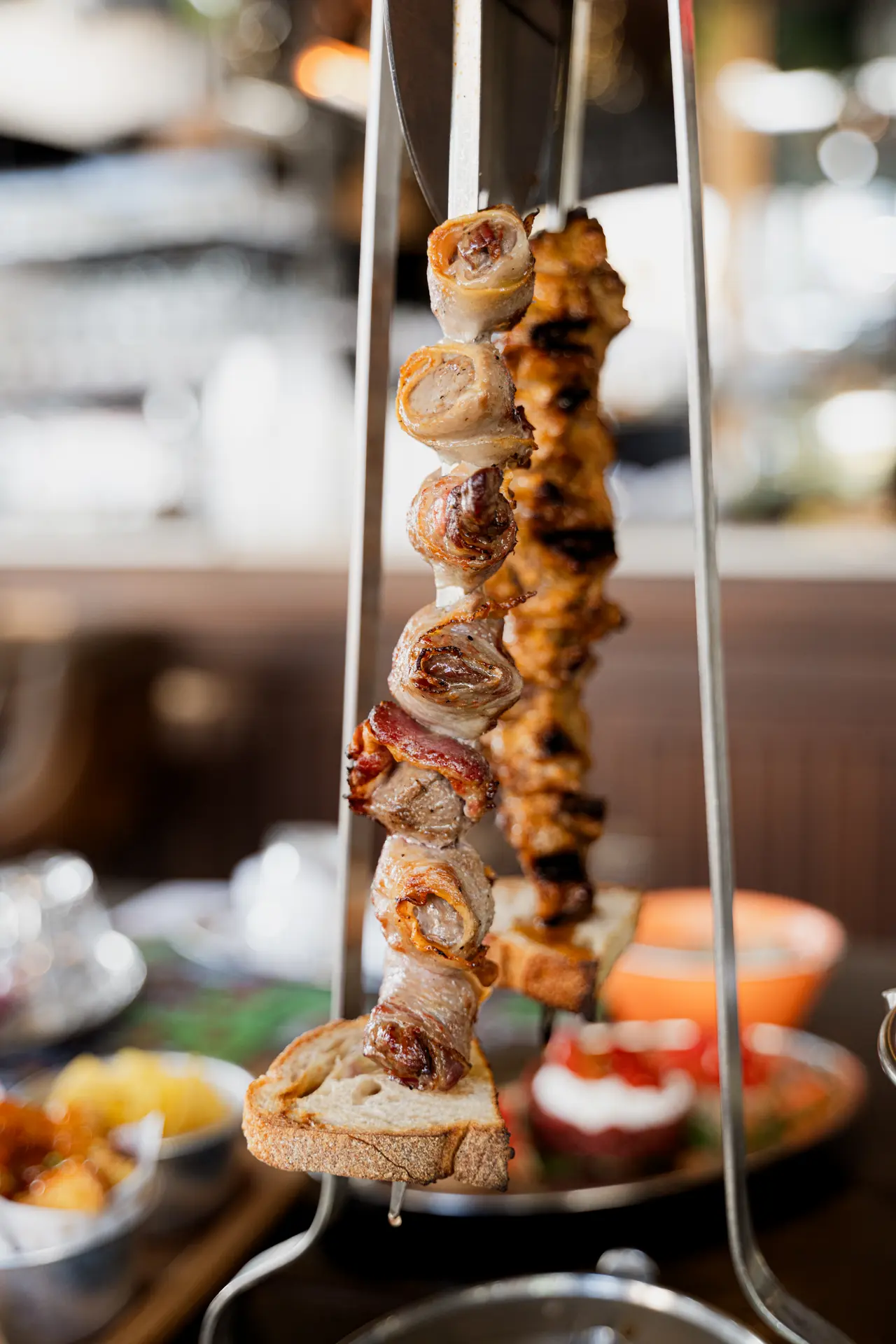 Due spade appese al supporto sopra il tavolo, una di carne avvolta nel guanciale e una di pollo