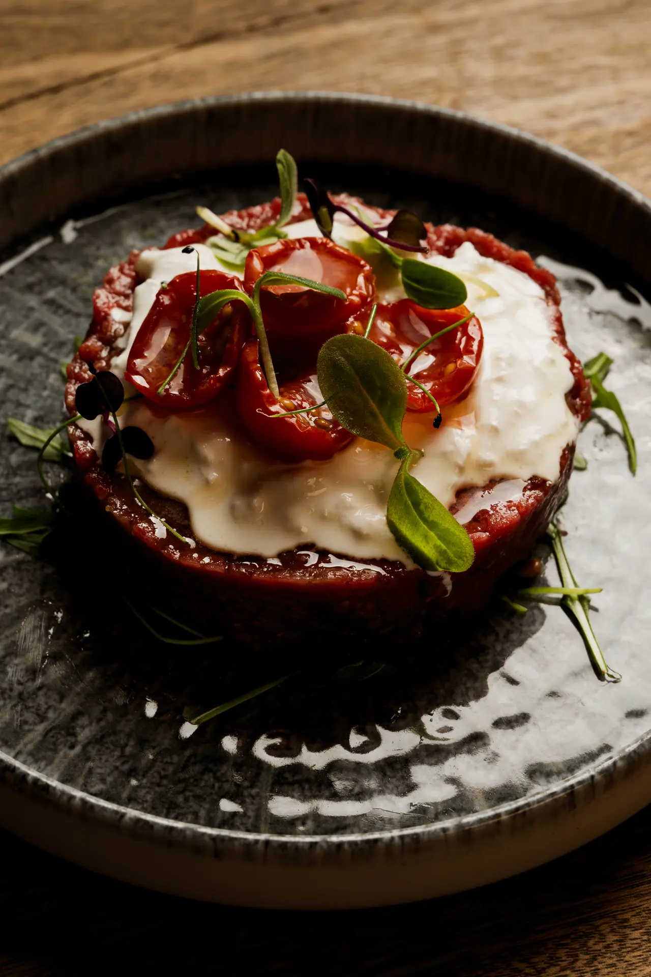 Tartare di manzo con burrata e pomodorini appassiti, servita su un piatto scuro