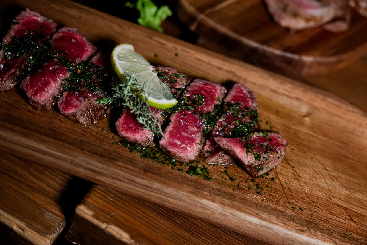 Tagliata di manzo affettata su un tagliere di legno, con lime e erbe